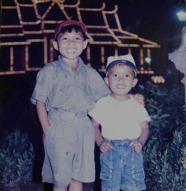 Nov Sochetra and their brother as children, smiling at night before a lit pavilion